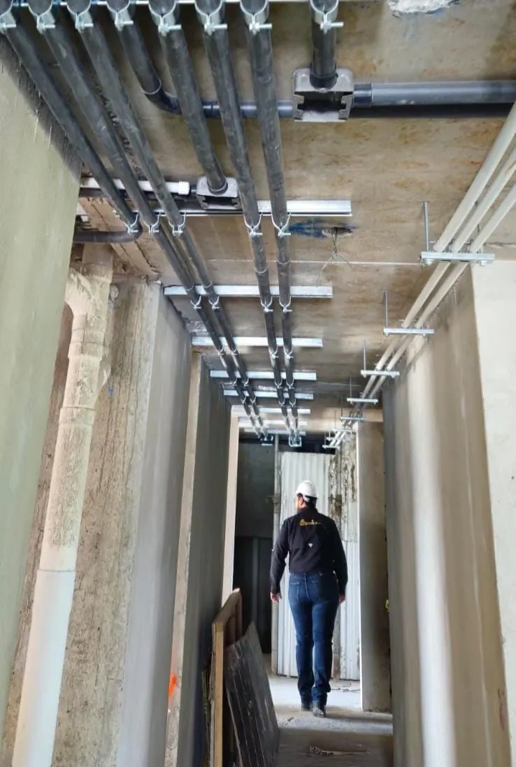 Pasillo en obra con la canalización eléctrica instalada en el techo y un supervisor de FESICA al fondo